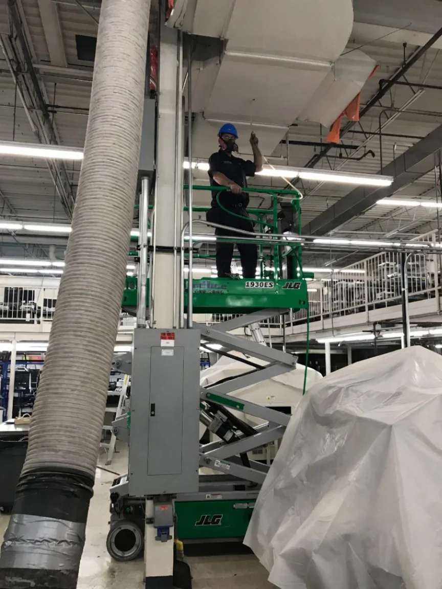 Technician on a scissor lift cleaning large ductwork in an industrial facility