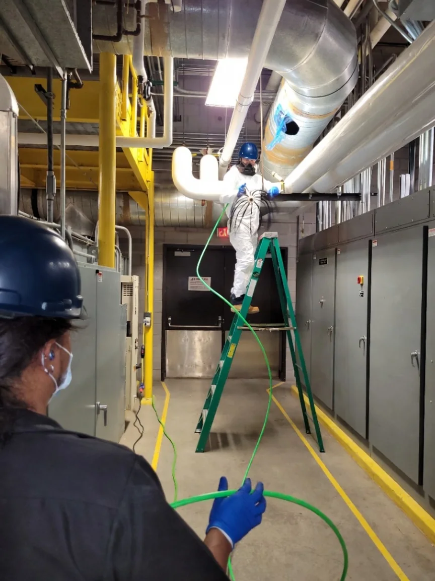 Crew cleaning insulated ductwork in a commercial mechanical room